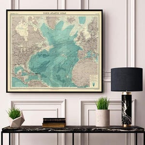 May include: Framed vintage map of the North Atlantic Ocean, featuring detailed cartography in shades of teal, beige, and gray. The map is displayed in a black frame, adding a classic touch to the wall decor. The title "North Atlantic Ocean" is visible at the top.
