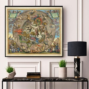 Könnte beinhalten: Gerahmter Vintage-Himmelskartendruck. Das Kunstwerk zeigt eine detaillierte Illustration der Sternbilder mit Figuren und Fabelwesen. Die Farbpalette umfasst Blau-, Gelb- und Brauntöne. Der Druck wird auf einem schwarzen Marmortisch mit einer Lampe und Topfpflanzen ausgestellt.