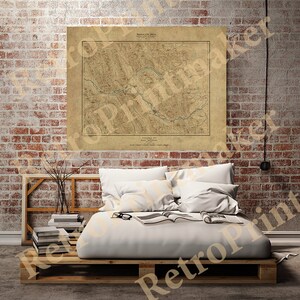 May include: An antique map of the Shenandoah Valley in Virginia, printed on aged paper with a brown background. The map shows the Shenandoah River winding through the valley, with mountains and towns marked in detail. The map is framed and hanging on a brick wall above a bed with white linen.