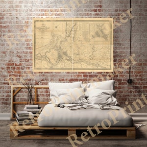 May include: A vintage map of the city of Philadelphia, Pennsylvania, printed on aged paper with a light brown background. The map shows the city's streets, rivers, and landmarks. The map is framed and hanging on a brick wall above a bed with white linens.