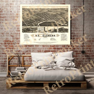 May include: An antique map of Mt. Clemens, Michigan, showing the city's layout and key landmarks. The map is printed in black and white and features a detailed illustration of the city's streets, buildings, and waterways. The map is framed and displayed on a brick wall.