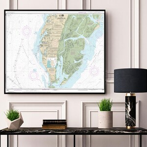 Puede incluir: Un mapa náutico enmarcado de la Bahía de Chesapeake, Virginia, con marcas detalladas y un esquema de color verde y marrón. El mapa está colgado en una pared blanca sobre una mesa consola negra con una lámpara, plantas en macetas y libros.