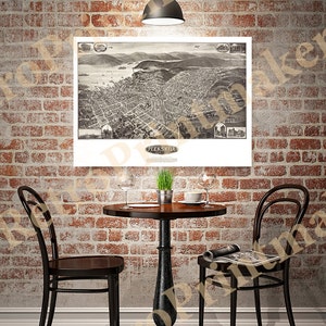 May include: A black and white vintage map of Peekskill, New York, framed and hanging on a brick wall above a small round table with two chairs. The table has a brown top and black metal legs. There is a potted plant on the table.