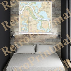 May include: A nautical chart of the waters around the entrance to the harbor of the city of Seattle, Washington. The chart is printed on paper and has a light blue background with dark blue lines and text. The chart is framed and hanging on a wall above a bed.