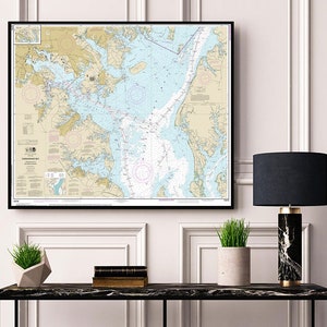 Może przedstawiać: Ramka z mapą nawigacyjną Zatoki Chesapeake, z dokładnymi oznaczeniami i czarną ramą. Mapa wisi na białej ścianie z białymi listwami i ozdobami. Czarna marmurowa lampa z czarnym abażurem stoi na czarnym stole z doniczką i książkami.