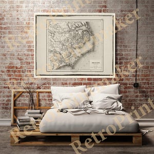 May include: A vintage map of the coast of the Carolinas, printed in black and white on a cream-colored paper. The map is framed and hanging on a brick wall above a bed with white bedding.