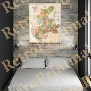 May include: A vintage map of the Republic of Mexico, printed in black and white with colored borders, hangs on a wood-paneled wall above a white bed with two pillows. The map is framed and has a title at the top.