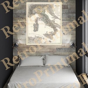 May include: A vintage map of Italy, printed in black and white, with a beige background. The map is framed and hanging on a wall above a bed with white linens. The wall is made of wood planks.