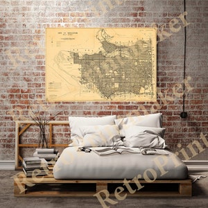 May include: A vintage map of Vancouver, British Columbia, Canada, printed on cream-coloured paper. The map shows the city's streets, parks, and other features. The map is framed and hanging on a brick wall.