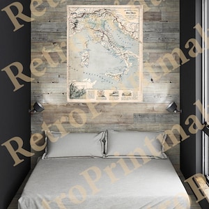 Op de afbeelding: Een vintage kaart van Italië, gedrukt in zwart-wit met gekleurde accenten, is ingelijst en hangt aan een houten muur boven een bed met witte lakens. De kaart is getiteld "Della Italia" en toont de regio's van Italië.