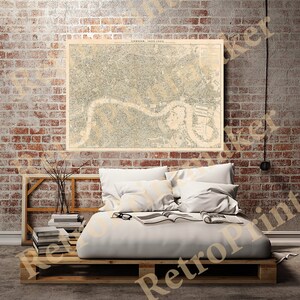 May include: A vintage map of London, England, from 1893-1903, printed in black and white on a cream-colored paper. The map is framed and hanging on a brick wall above a bed with white bedding.