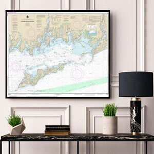 Puede incluir: Un mapa náutico enmarcado de las aguas alrededor de Long Island Sound, Nueva York. El mapa está en blanco y negro con acentos azules y verdes. El mapa está enmarcado en un marco negro y está colgado en una pared blanca. Una lámpara negra con una pantalla negra está sobre una mesa negra con una planta en una maceta gris.
