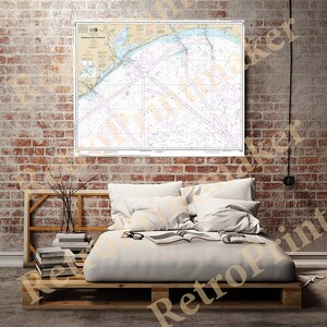 May include: A nautical chart of the Great Lakes, showing the coastline of Michigan, Wisconsin, and Ontario. The chart is printed on a white background with blue lines and text. The chart is framed and hanging on a brick wall above a bed with white bedding.