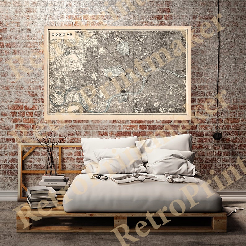 May include: A vintage map of London, England, printed in black and white with brown accents. The map is framed and hanging on a brick wall above a bed with white bedding.