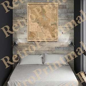 May include: A vintage map of the Caucasus region, printed on aged paper, hangs on a wood-paneled wall above a white bed with two pillows. The map is framed and features a title in Cyrillic script.