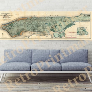 May include: A vintage map of New York City, printed on paper with a cream background. The map shows the city's streets and landmarks, including the East River and the Hudson River. The map is framed and hanging on a white brick wall above a gray couch.
