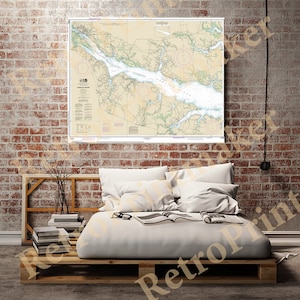 May include: A vintage nautical chart of the Chesapeake Bay, printed on paper with a cream background and green and brown details. The chart is framed and hanging on a brick wall above a wooden bed with white bedding.