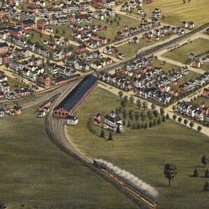 May include: An aerial view of a train station with a large train shed and multiple tracks. The station is surrounded by a residential neighborhood with houses and trees. A train is pulling out of the station with smoke billowing from the engine.