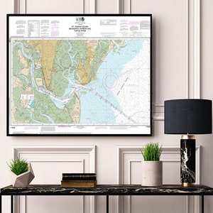 May include: A framed nautical chart of St. Simons Sound, Brunswick Harbor, and Turtle River. The chart features detailed depictions of waterways, landmasses, and navigational markers, with a color palette of blues, greens, and tans. The frame is black.