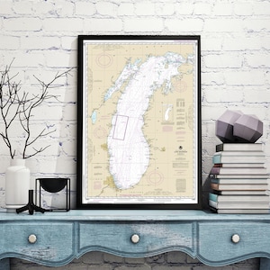 May include: A framed nautical chart of Lake Michigan with detailed markings and a black frame. The chart is displayed on a light blue dresser with a white vase and a black metal sculpture.