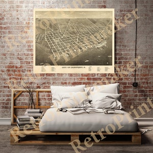 May include: A sepia-toned vintage map print of Sandusky, Ohio, featuring a detailed aerial view of the city's layout, streets, and waterfront. The map is framed and displayed on a brick wall, with a bed and decor in the foreground.