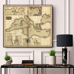 Puede incluir: Mapa antiguo enmarcado del mar Mediterráneo, con líneas costeras y características geográficas detalladas. El mapa está en un marco negro y cuelga de una pared blanca. El mapa tiene un fondo beige con detalles en rojo y verde.