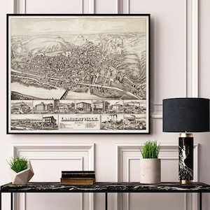 May include: A vintage black and white map of Lambertville, New Jersey, framed in a black frame and hanging on a white wall above a black console table with a black and white marble lamp, a potted plant, and a stack of books.