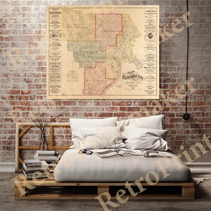 May include: An antique map of Floyd County, Indiana, showing the county's townships and cities. The map is printed on aged paper and has a vintage aesthetic. It is framed and hanging on a brick wall above a bed with white bedding.