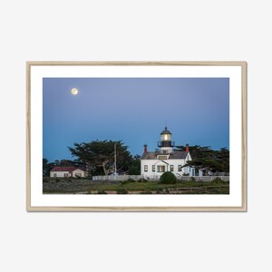 May include: A white lighthouse with a black roof and a light on top, surrounded by trees and a full moon in the sky.
