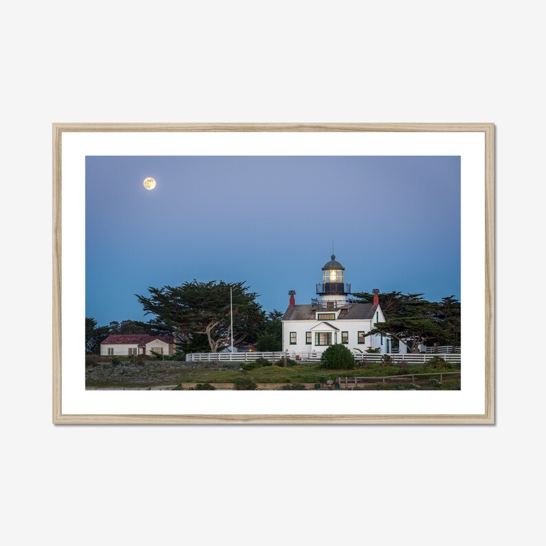 May include: A white lighthouse with a black roof and a light on top, surrounded by trees and a full moon in the sky.