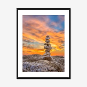 May include: A stack of gray stones balanced on top of each other against a backdrop of a colorful sunset sky.