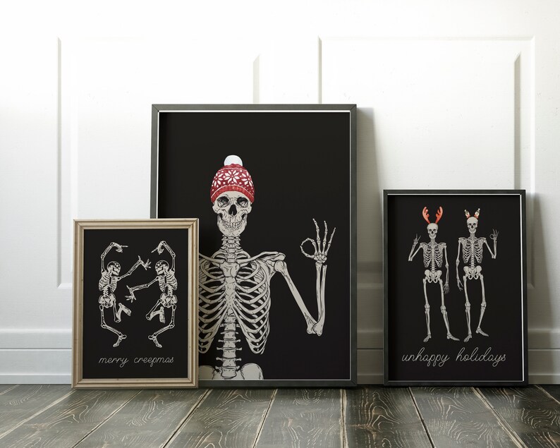 Op de afbeelding: Drie ingelijste wandposters met skeletten op een zwarte achtergrond. De linker poster toont twee dansende skeletten met de tekst "merry creepmas". De middelste poster toont een skelet met een rode gebreide muts. De rechter poster toont twee skeletten met een gewei en de tekst "unhappy holidays".