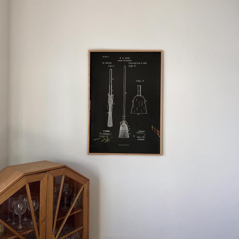 May include: A framed print featuring a broom patent design in black and white. The print shows detailed diagrams of a broom, dustpan, and related parts, with technical annotations and patent details. The frame is made of natural wood.