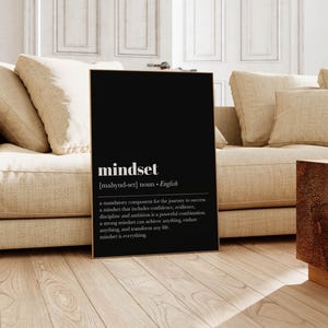 K&ouml;nnte beinhalten: Ein schwarzer gerahmter Druck mit dem Wort "mindset" in wei&szlig;em Text. Der Druck enth&auml;lt eine Definition des Wortes mit dem Text "a mandatory component for the journey to success..." Der Druck wird in einem Wohnzimmer gezeigt.