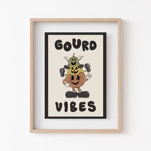 K&ouml;nnte beinhalten: Ein gerahmter Druck mit dem Text "GOURD VIBES" in schwarzen Buchstaben. Der Druck zeigt eine Cartoon-Illustration von drei &uuml;bereinander gestapelten K&uuml;rbissen mit l&auml;chelnden Gesichtern.