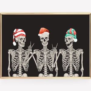 May include: A framed wall art print featuring three skeletons against a solid black background. The skeletons wear festive hats: one in red and white stripes, one in red with a white trim, and one in green and red. They pose with hand gestures.