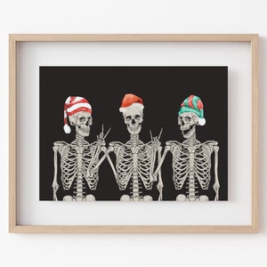 May include: A framed art print featuring three skeletons against a black background. Each skeleton wears a different Christmas-themed hat: one with red and white stripes, one solid red, and one with green and red stripes. The skeletons are gesturing.