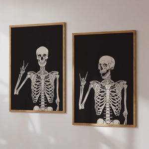 K&ouml;nnte beinhalten: Zwei gerahmte Wandbilder mit cremefarbenen menschlichen Skeletten vor einem einfarbigen schwarzen Hintergrund. Das linke Skelett zeigt mit der rechten Hand ein Friedenszeichen, w&auml;hrend das rechte Skelett mit der rechten Hand ein Rock-Symbol formt.