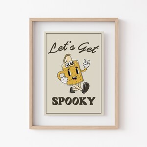 K&ouml;nnte beinhalten: Ein beigefarbener gerahmter Druck mit einer Cartoon-Illustration einer gruseligen, l&auml;chelnden, gelben Flasche mit Augen und schwarzem Umriss. Der Text "Let's Get Spooky" ist in Schwarz unter der Flasche gedruckt.