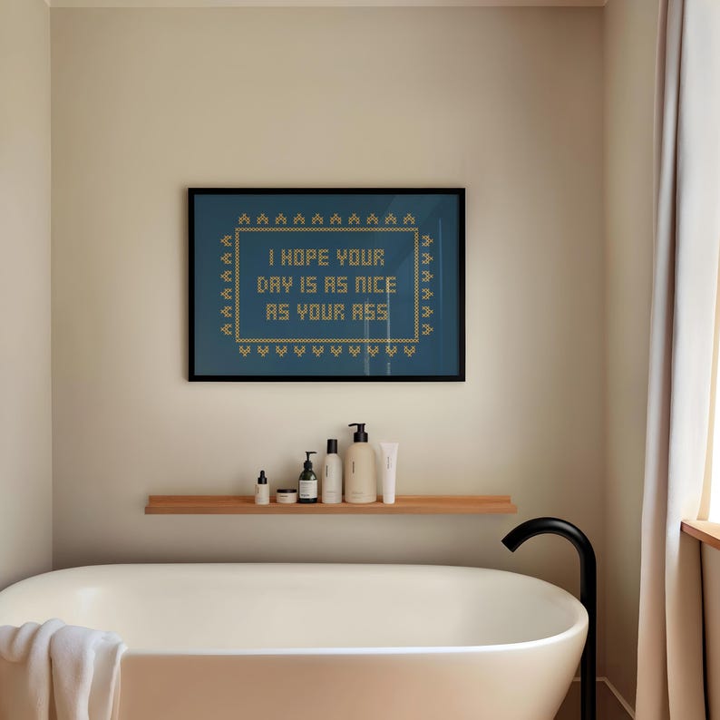 May include: A framed art print with the text "I HOPE YOUR DAY IS AS NICE AS YOUR ASS" in a cross-stitch style. The print is displayed above a bathtub with toiletries on a shelf.