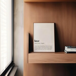 May include: A framed print with the word "love" in a minimalist design. The definition of love is printed below the word. The print is displayed on a wooden shelf with books.