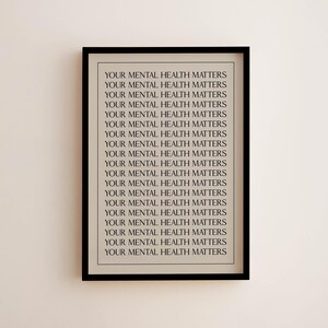 May include: A framed print with the repeated text "YOUR MENTAL HEALTH MATTERS" in a black frame. The text is in a simple, sans-serif font, and the background is a light beige colour. The print is displayed on a light beige wall.