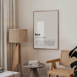 May include: A framed print with the word "love" in a minimalist design. The definition of love is printed below the word. The print is in a room with a wooden floor lamp, a small side table, and a wooden chair.