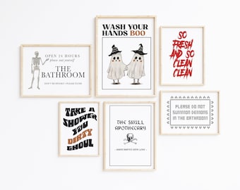May include: A collection of framed Halloween-themed art prints. The prints feature spooky text and illustrations, including ghosts, skeletons, and phrases like "Wash Your Hands Boo" and "The Bathroom". The frames are a light wood color.