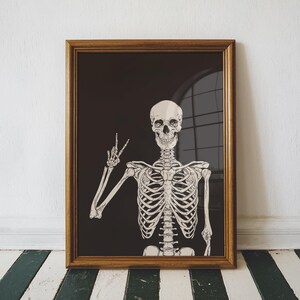 K&ouml;nnte beinhalten: Ein gerahmter Kunstdruck mit einer detaillierten Illustration eines menschlichen Skeletts vor einem einfarbigen schwarzen Hintergrund. Das Skelett ist ab dem Oberk&ouml;rper dargestellt, wobei der rechte Arm erhoben ist und die Finger ein Friedenszeichen formen.