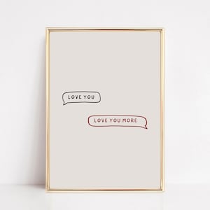 May include: A framed print with a gold border. The print features two speech bubbles with the phrases "LOVE YOU" and "LOVE YOU MORE" in black and red text, respectively, on a light beige background.