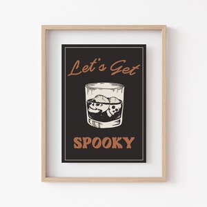 K&ouml;nnte beinhalten: Ein gerahmter Druck mit schwarzem Hintergrund und wei&szlig;em Text, der "Let's Get Spooky" lautet. Der Druck zeigt eine Zeichnung eines Glases mit Eisw&uuml;rfeln, die wie Sch&auml;del aussehen.