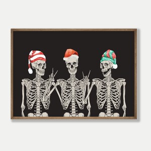 May include: A framed wall art print featuring three skeletons against a solid black background. Each skeleton wears a different holiday hat: one with red and white stripes, one solid red, and one with green and red stripes, all with white pom-poms.