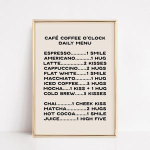 May include: A framed print with a beige background and gold frame. The text "CAFÉ COFFEE O'CLOCK DAILY MENU" is at the top, followed by a list of coffee drinks and the number of smiles, hugs, kisses, and high fives associated with each.