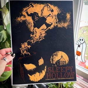 Peut inclure: Une impression noire et orange du Cavalier sans t&ecirc;te chevauchant un cheval avec une citrouille au premier plan. Le texte "Sleepy Hollow" est en bas au centre de l'impression. Une collaboration Studio Katooween x Chris Garofalo.